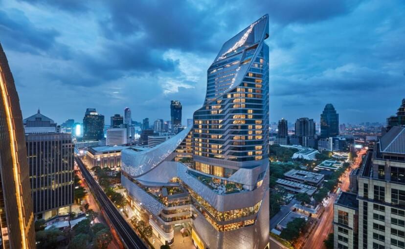 Beeindruckende Außenansicht des Park Hyatt Bangkok bei Abenddämmerung, mit futuristischer Architektur, beleuchteter Glasfassade und Blick auf die umliegende Skyline im zentralen Geschäftsviertel.