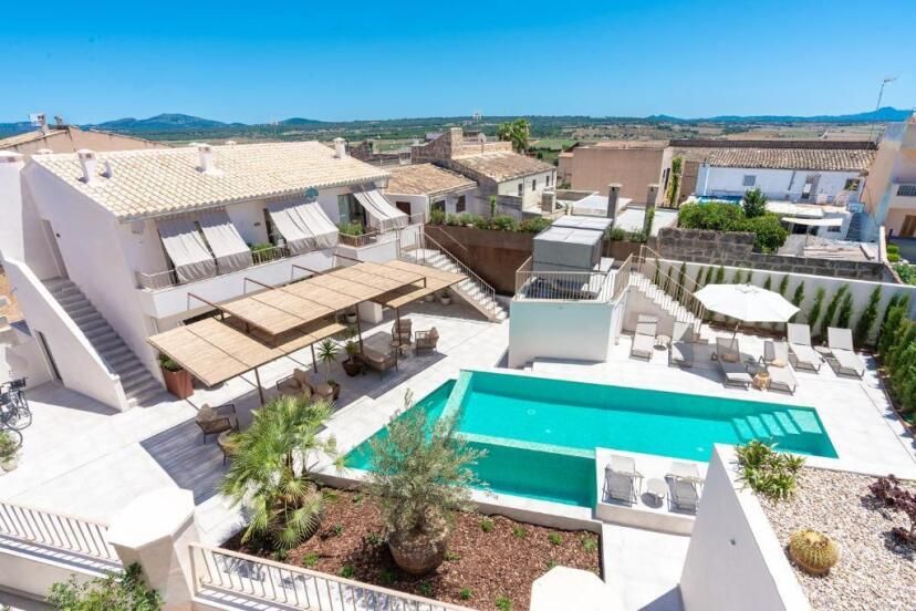 Lichtdurchfluteter Innenhof des Ynaira Hotel & Spa mit modernem Poolbereich, Sonnenschirmen, schattiger Pergola, weißen Gebäuden im mediterranen Stil und weitem Blick über die Landschaft Mallorcas.