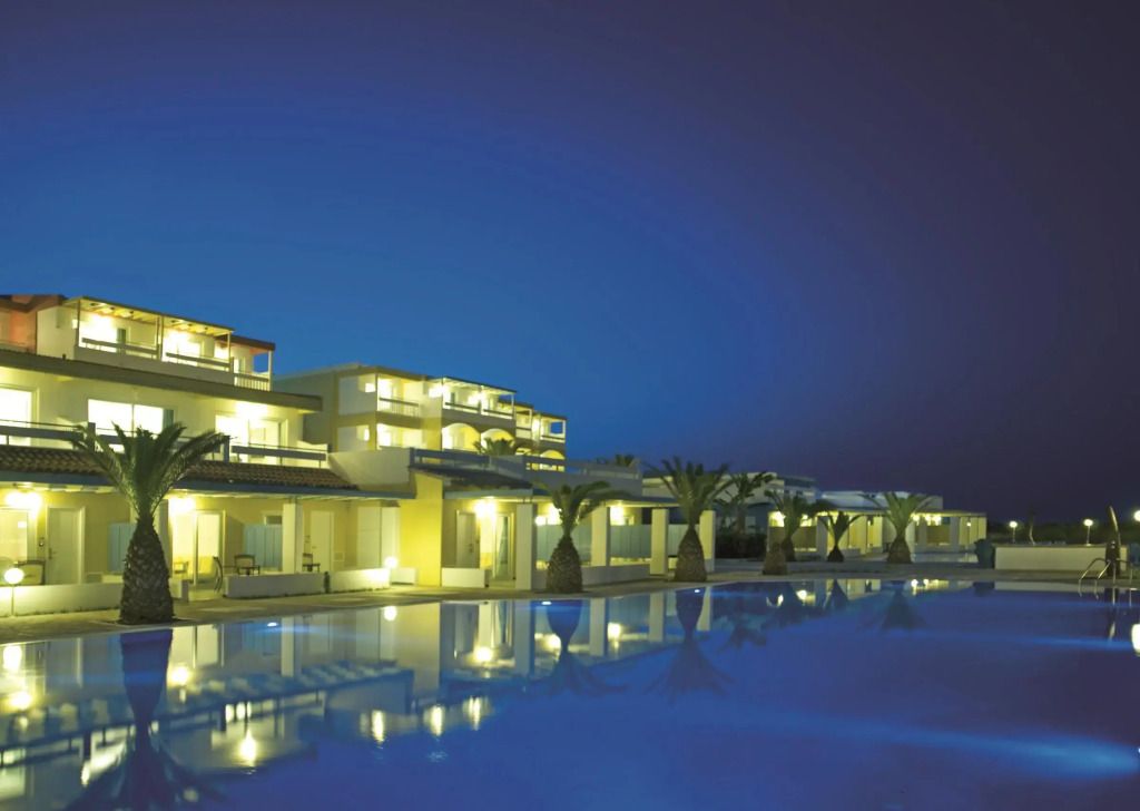 Hotelgebäude bei Nacht mit beleuchtetem Pool und Palmen