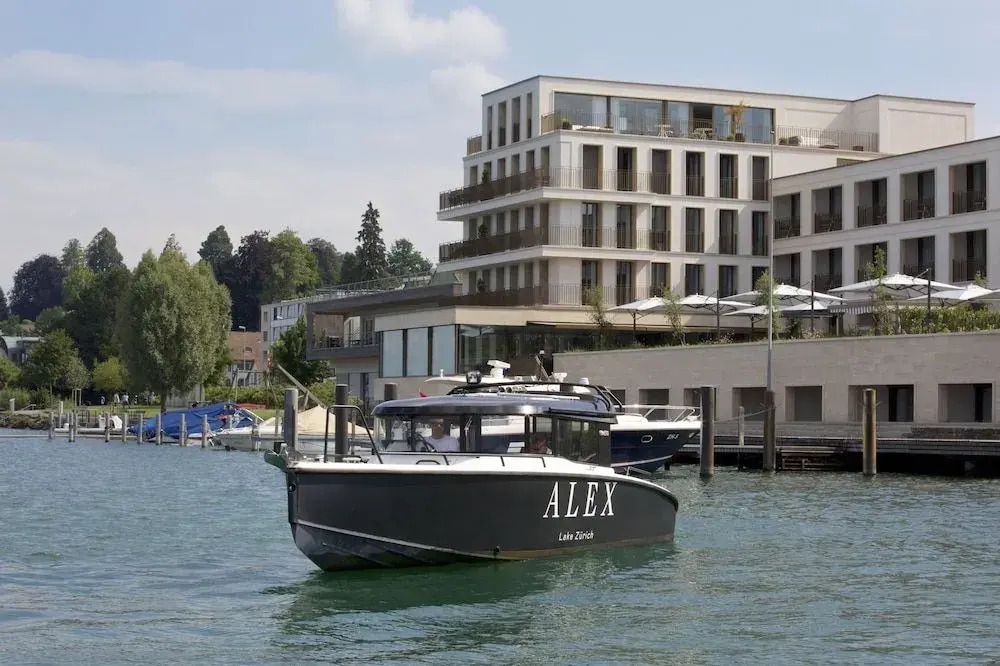 Außenansicht des Hotels Alex Lake Zurich mit einem Boot im Vordergrund