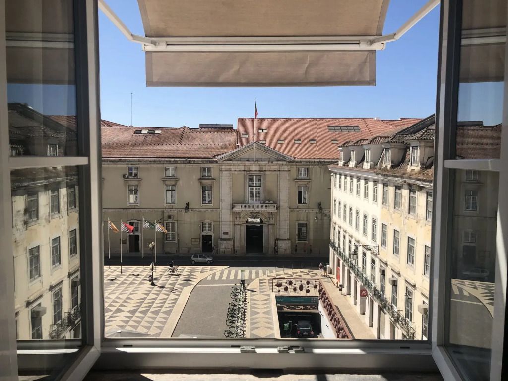 Ausblick von einem Fenster auf historischen Platz in Lissabon mit Flaggen und Gebäude.
