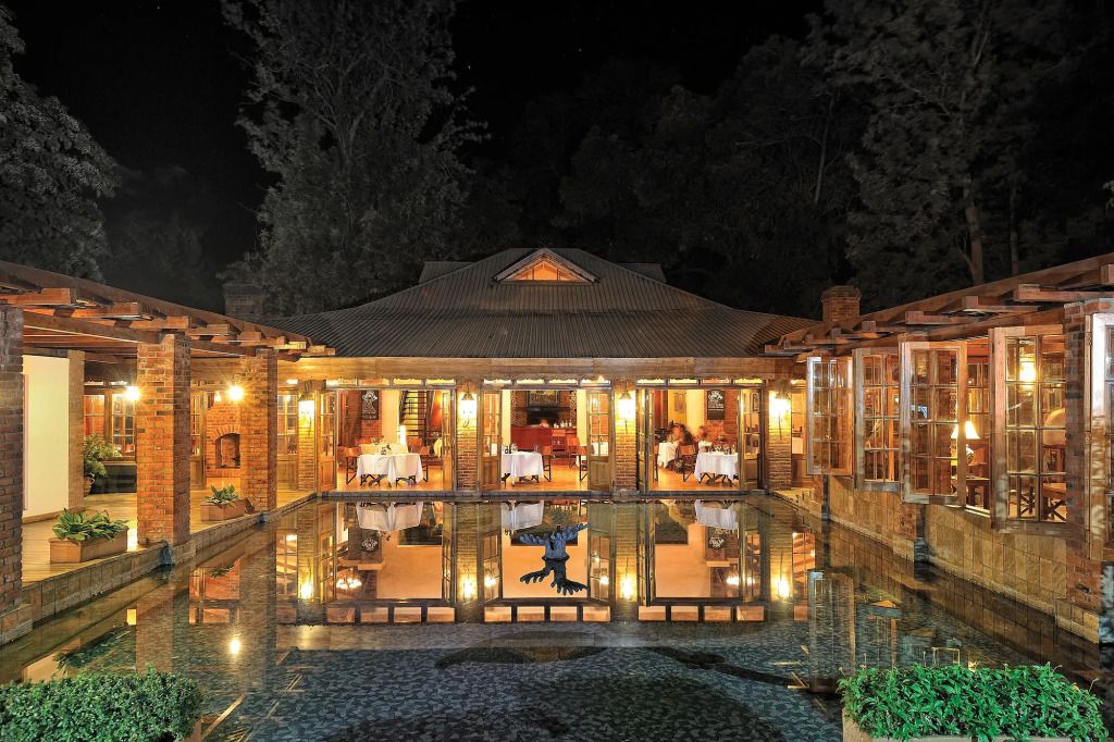 Elegantes Restaurant von außen mit beleuchtetem Teich bei Nacht im Arusha Coffee Lodge