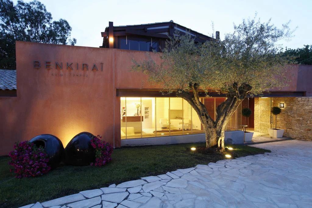 Außenansicht des Hotels mit beleuchtetem Eingang und Olivenbaum bei Nacht