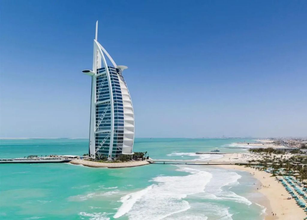 Burj Al Arab Hotel vor blauem Himmel und türkisfarbenem Wasser