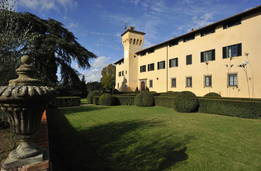 Historische Fassade des COMO Castello del Nero mit gepflegtem Garten im Vordergrund