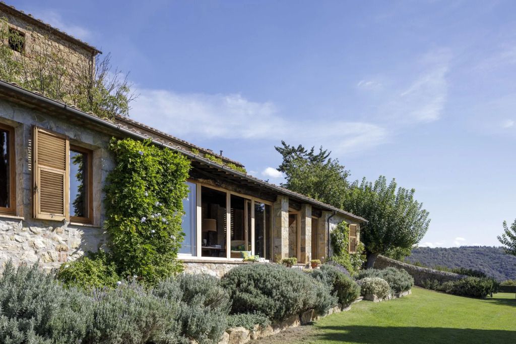 Steinhaus mit großen Fenstern und üppigem Garten unter blauem Himmel