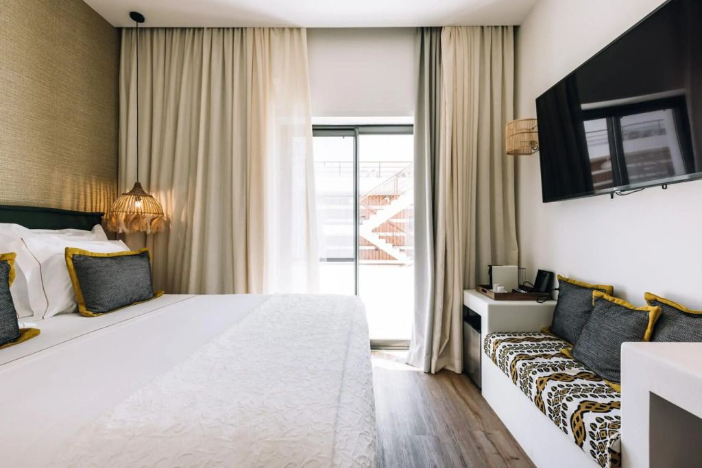 Elegantes Hotelzimmer mit großem Bett und Flachbildschirm, helle Vorhänge, warmes Licht.