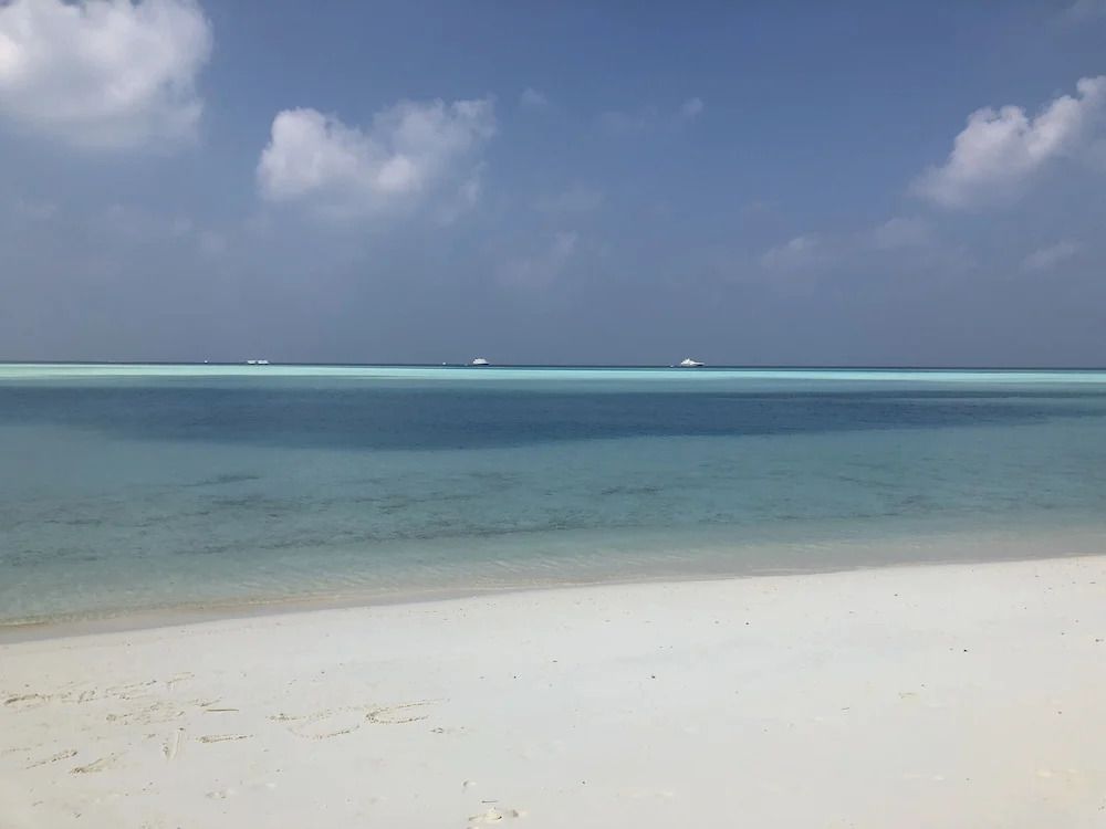Weißer Sandstrand am kristallklaren, blauen Meer unter einem wolkigen Himmel