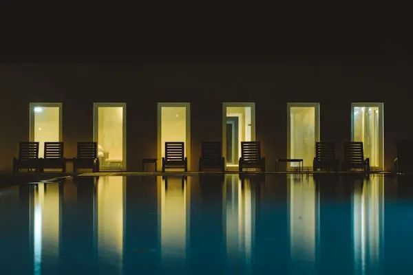 Pool mit beleuchteten Fensterfronten und Künstlerstuhl-Reflektionen im Wasser.