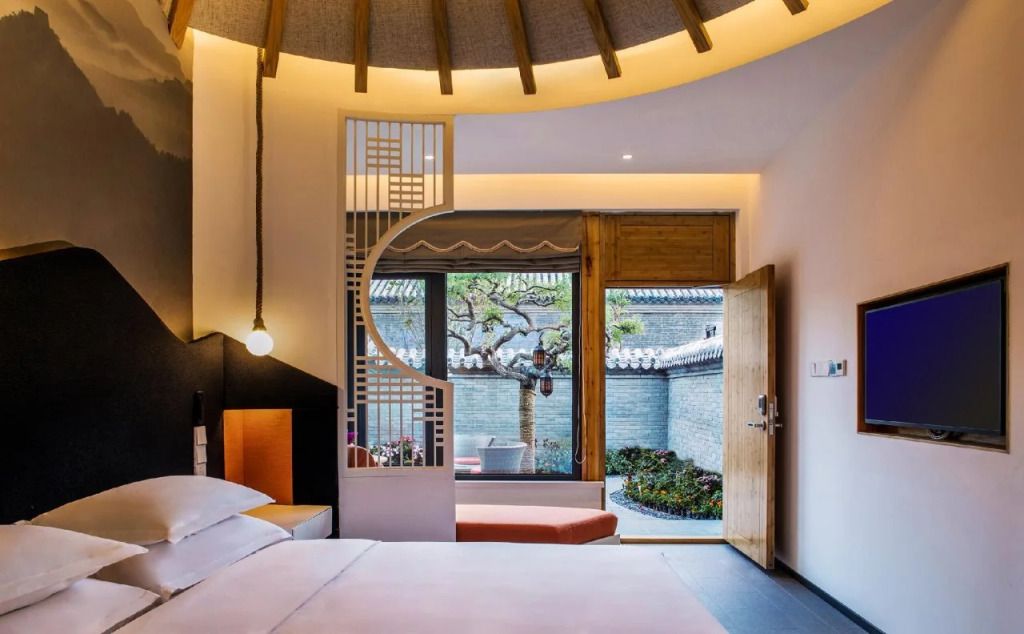 Modernes Hotelzimmer mit großer Fensterfront und dekorativem Baum im Hof.