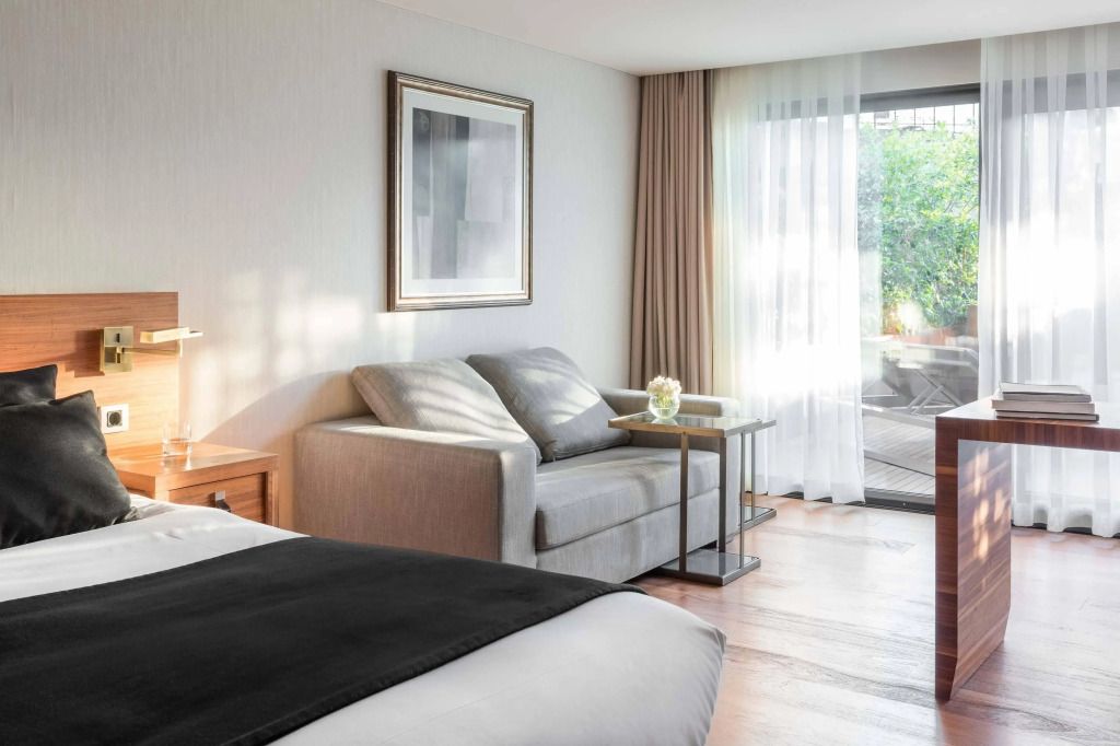 Helles Hotelzimmer mit bequemer Couch und Blick auf die Terrasse.