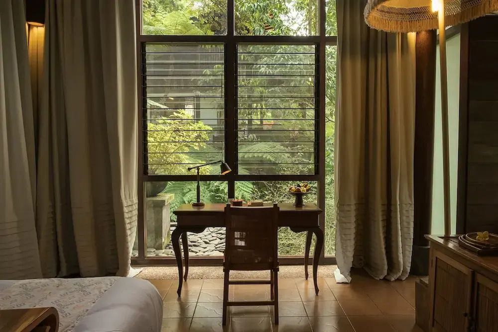 Schreibtisch am Fenster mit Blick auf einen grünen Garten im Resort.