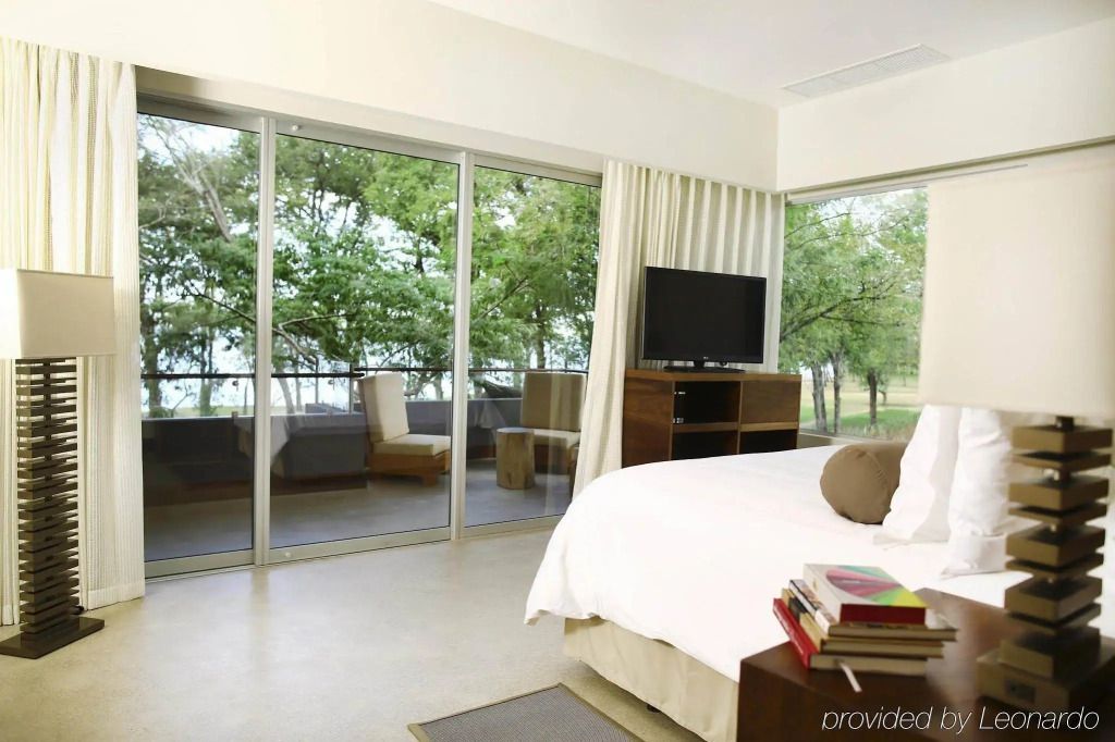 Helles Hotelzimmer mit großem Bett und Blick auf den Garten durch Glastüren