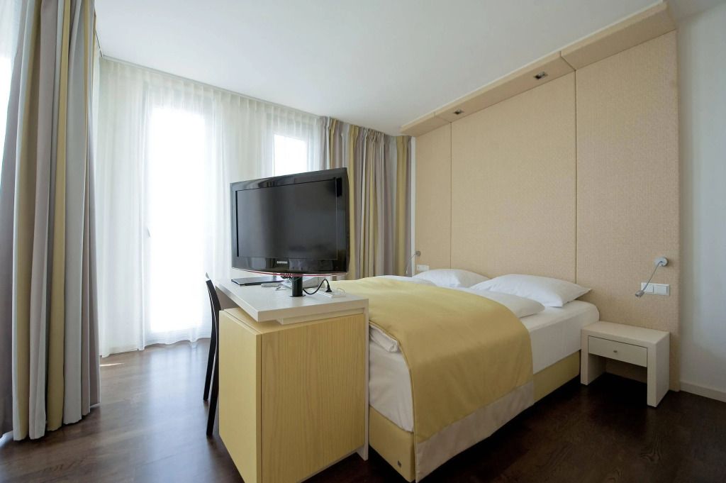 Helles Hotelzimmer mit Doppelbett und Flachbildfernseher