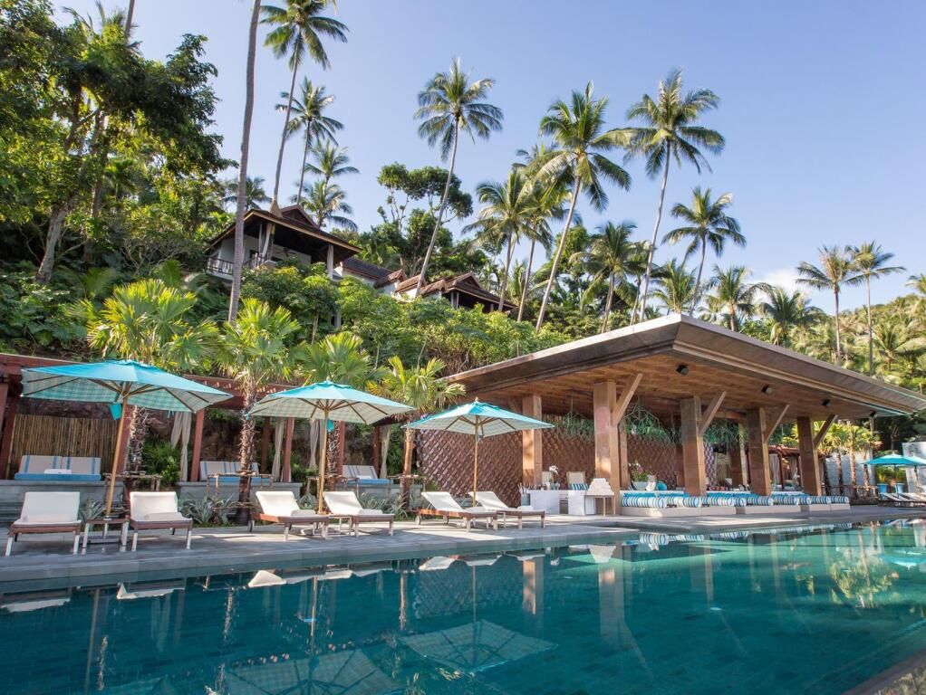 Infinity Pool mit Sonnenliegen und Sonnenschirmen umgeben von tropischen Palmen