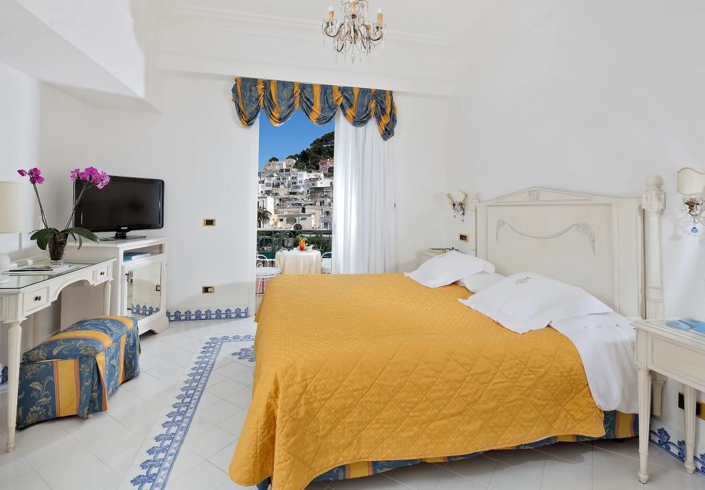 Helles Hotelzimmer mit gelber Tagesdecke und Aussicht auf die Stadt.