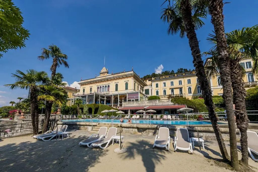 Außenansicht des Grand Hotel Villa Serbelloni mit Strand und Palmen.
