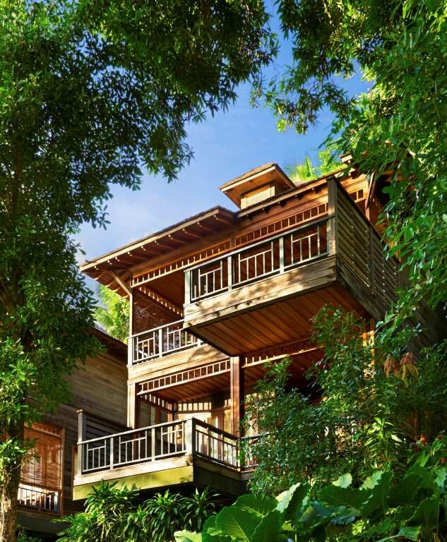 Dreistöckige Holzvilla umgeben von üppigem Grün mit überdachten Balkonen