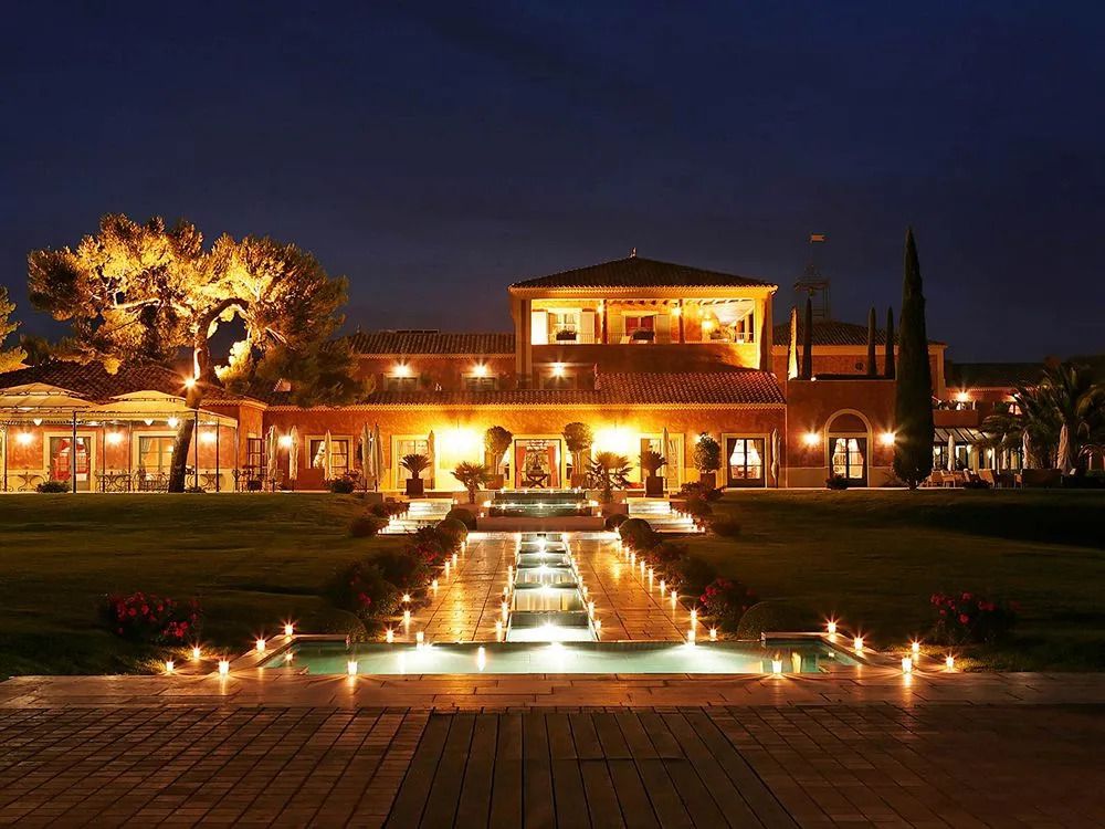 Hotelgebäude bei Nacht mit beleuchtetem Garten und Pool im Vordergrund