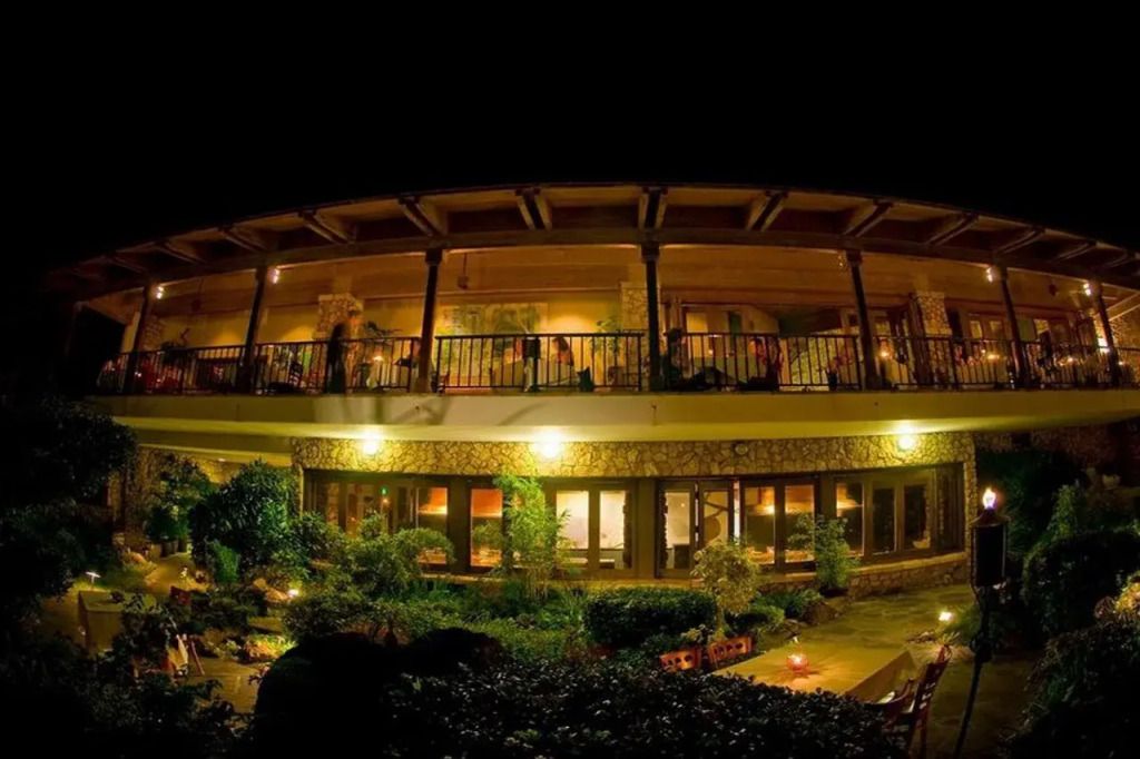 Nachtaufnahme eines Hotels mit beleuchteter Fassade und Pflanzen im Vordergrund