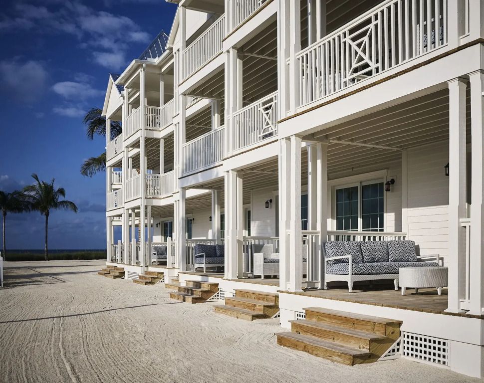 Strandansicht des Hotels mit weißen Balkonen und Holztreppen bei klarem Himmel