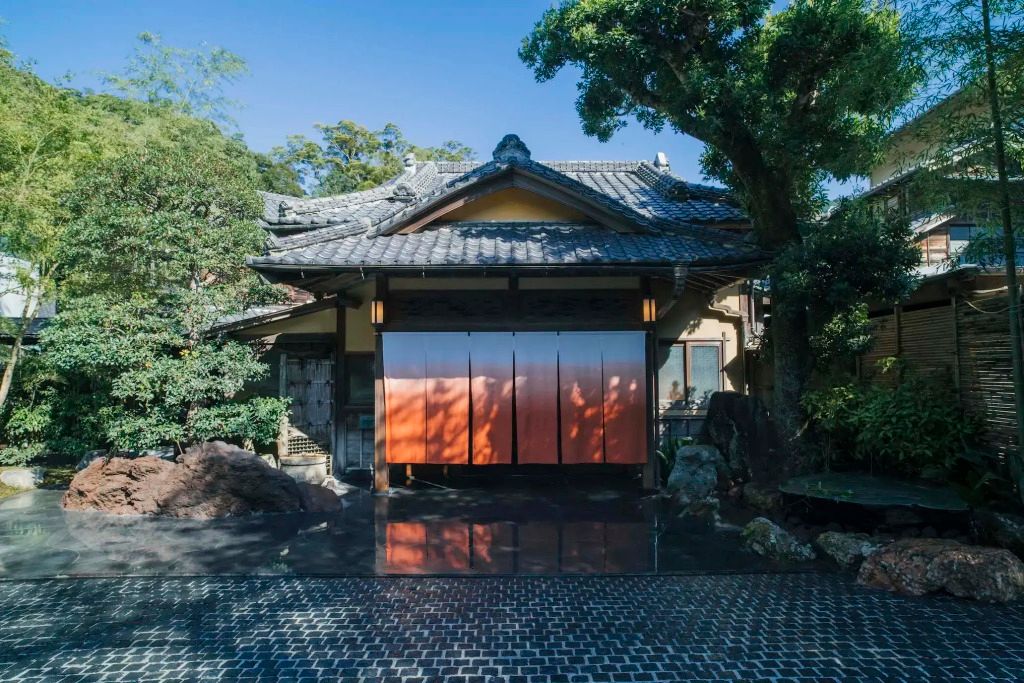 Traditionelle japanische Fassade mit Holzdach und großen Toren umgeben von Bäumen.