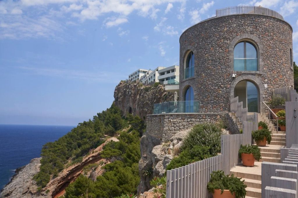 Hotelgebäude aus Stein eingebettet in eine Küstenlandschaft mit Meerblick.