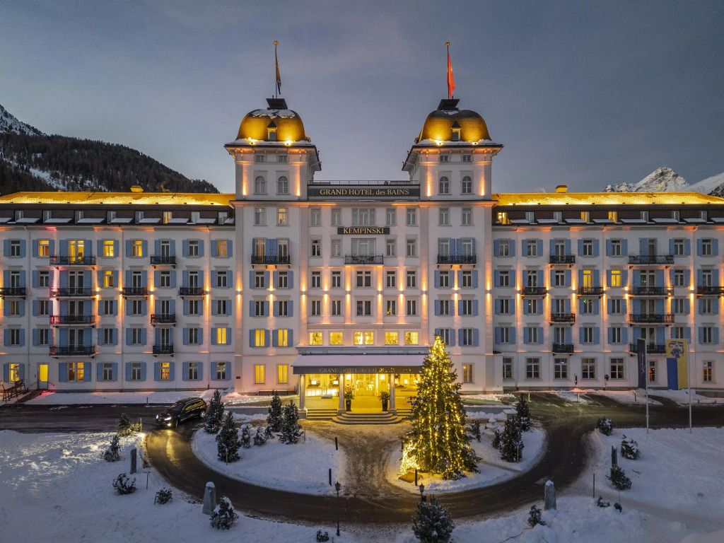 Beleuchtete Fassade des Grand Hotel des Bains Kempinski im Schnee bei Abenddämmerung