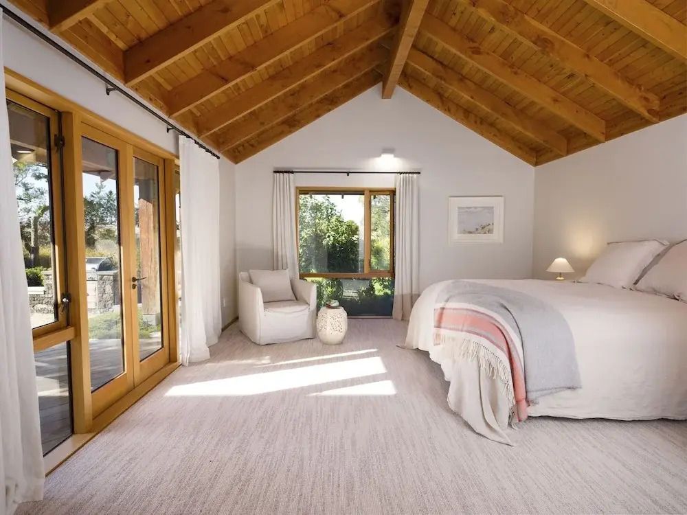 Gemütliches Schlafzimmer mit Holzbalkendecke und großem Fenster mit Gartenblick