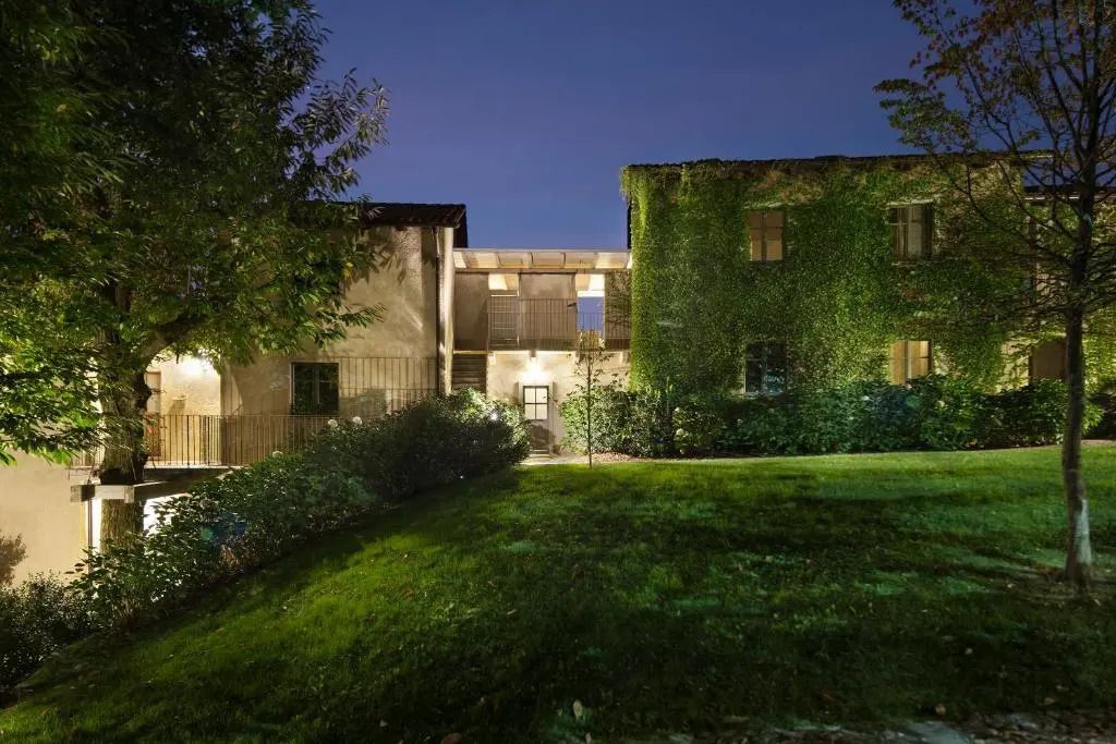 Nachts beleuchtete Hotelfassade mit begrünter Wand und gepflegtem Garten