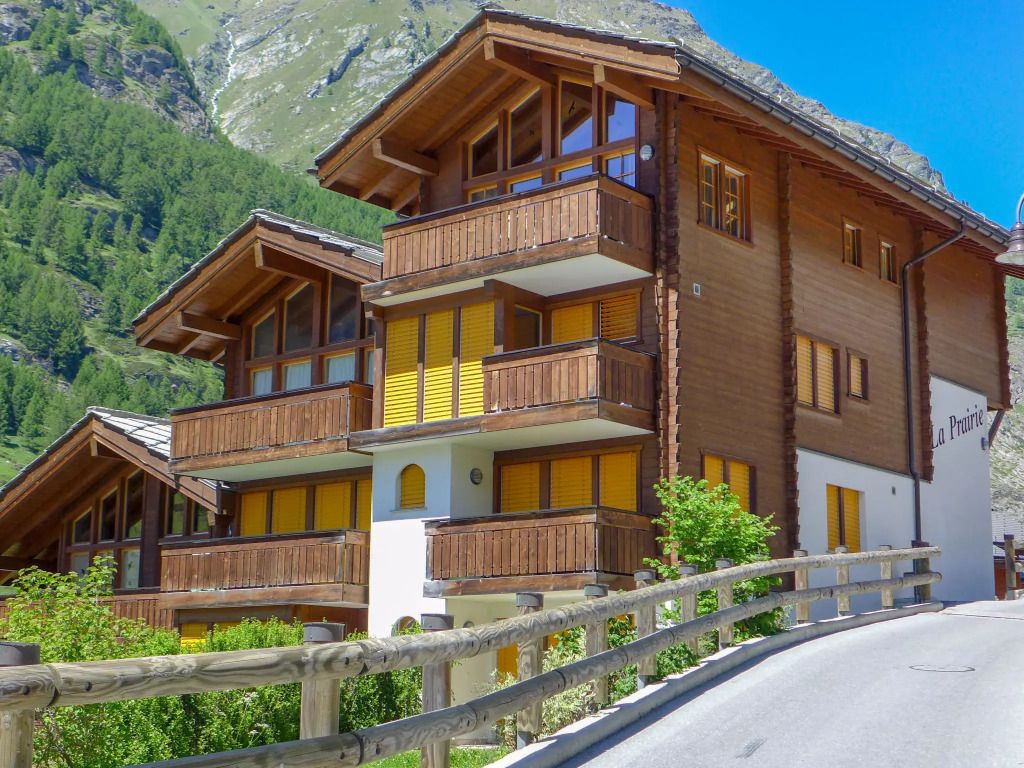 Alpenchalet mit Holzbalkonen und umliegenden Bergen an sonnigem Tag