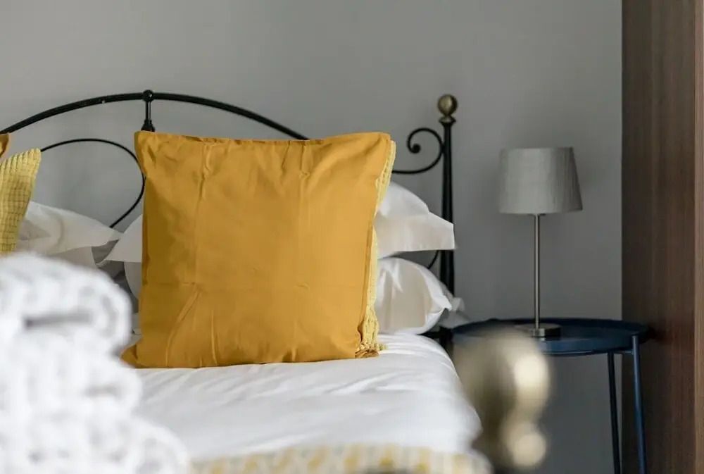 Blick auf ein Bett mit gelbem Kissen und Lampe im Hintergrund