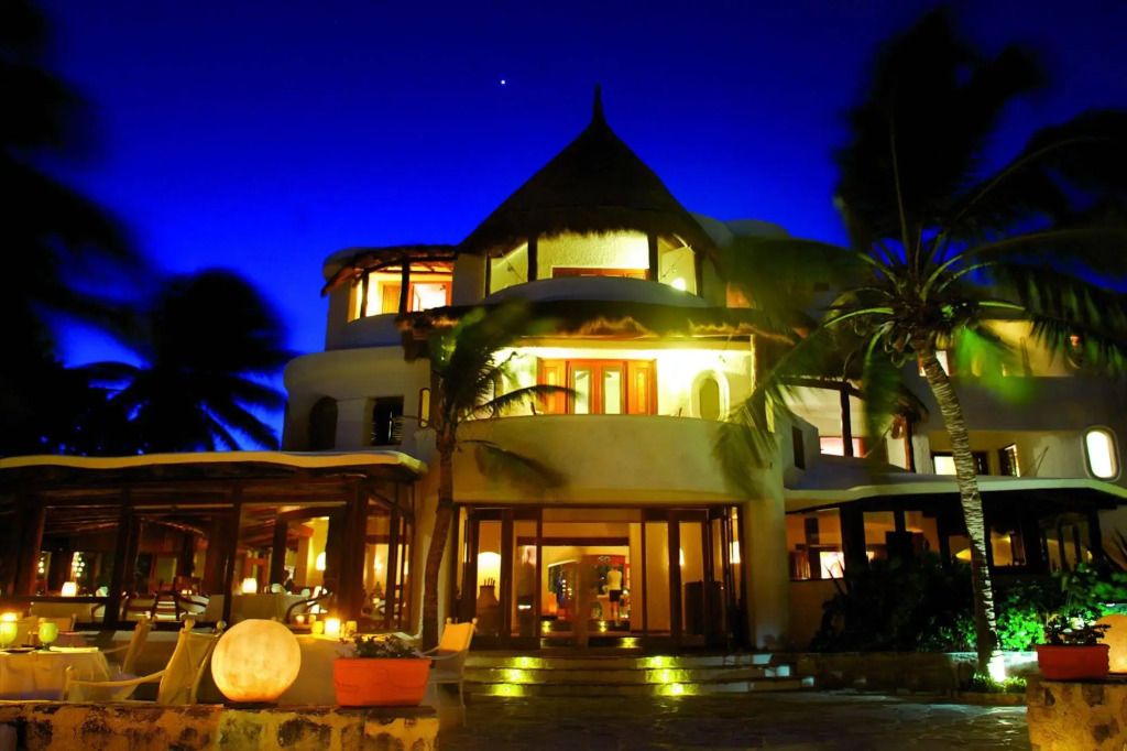 Beleuchtete Fassade des Hotels Maroma bei Nacht mit Palmen