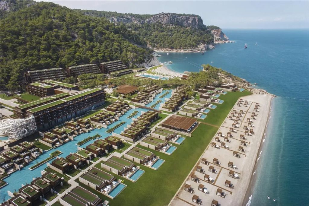 Luftaufnahme des MAXX Royal Kemer Hotels mit Pools und Meerblick inmitten grüner Hügellandschaft