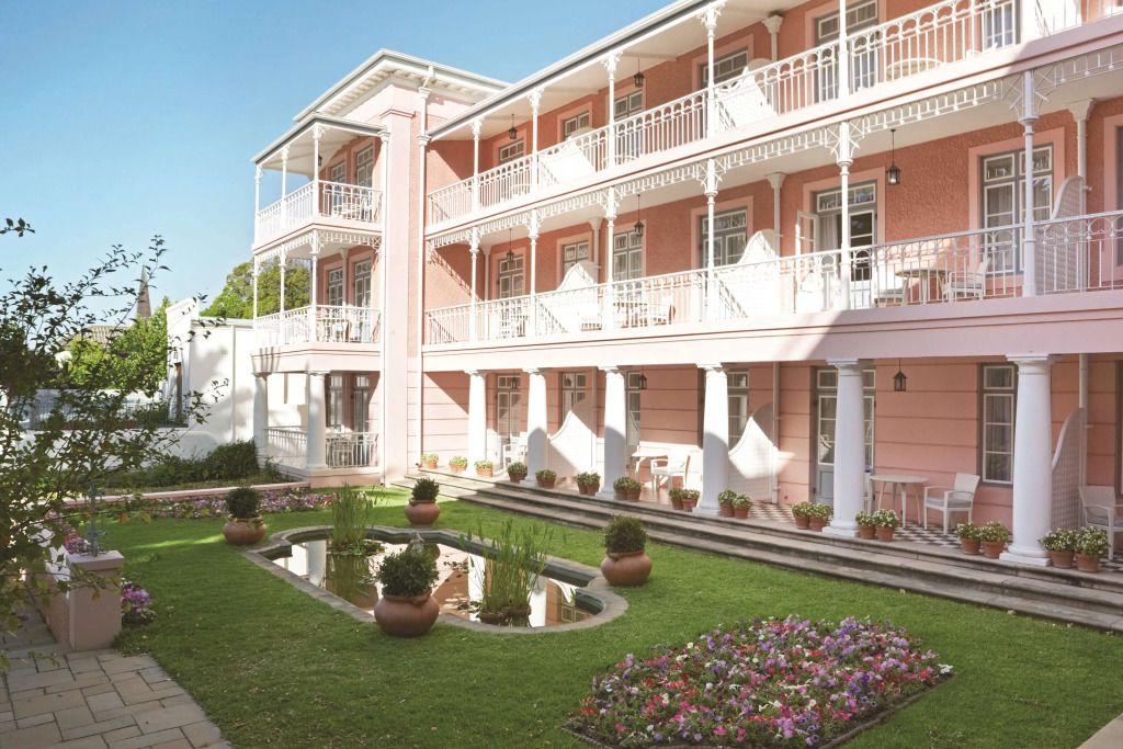 Klassische Fassade eines rosa Gebäudes mit Balkonen und gepflegtem Garten