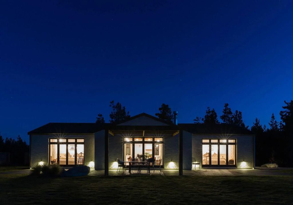 Außenansicht einer modernen Villa bei Nacht mit beleuchteten Fenstern und Tannen im Hintergrund