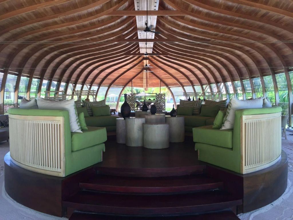 Eleganter Loungebereich mit geschwungener Holzdecke und grünen Sesseln