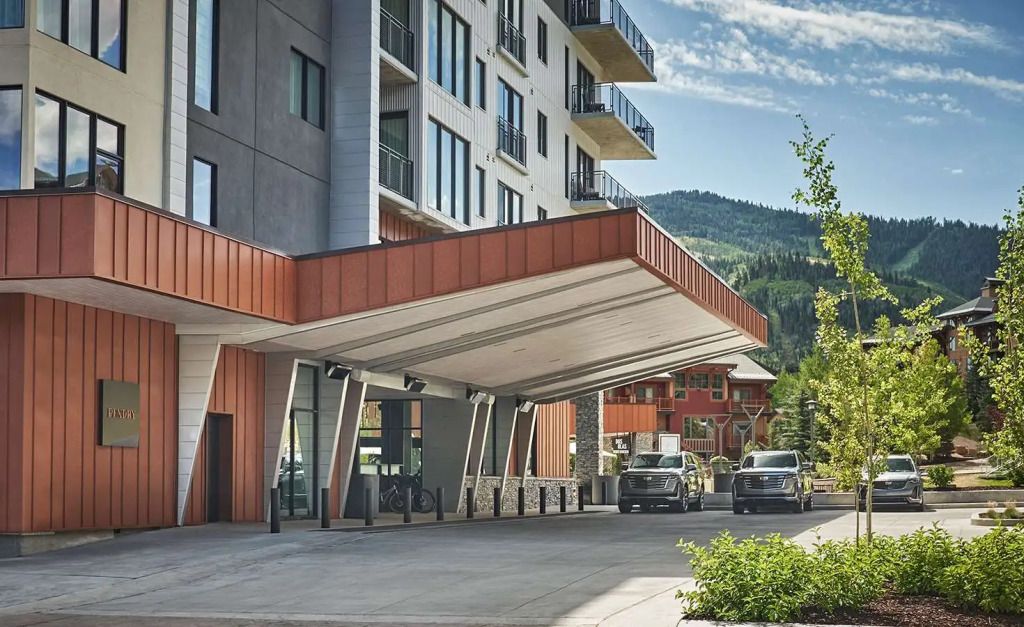 Moderne Hotelfassade mit überdachtem Eingangsbereich und Berglandschaft im Hintergrund