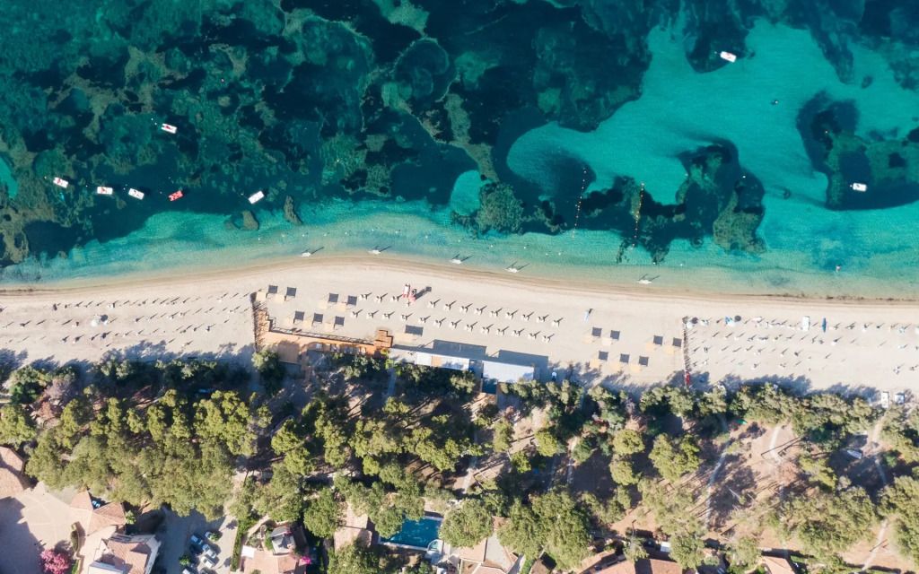 Luftaufnahme des Strandes mit kristallklarem Wasser und Sonnenschirmen