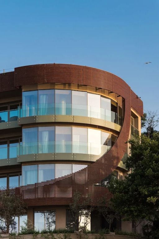 Moderne Hotelfassade mit gebogener Glasfront und Holzdetails unter blauem Himmel