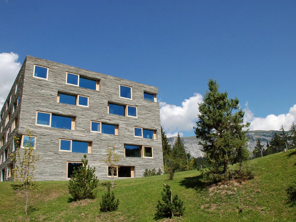 Außenansicht eines modernen Gebäudes aus Stein mit großen Fenstern, umgeben von grüner Landschaft