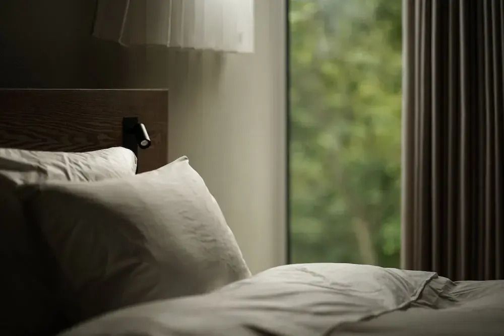 Gemütliches Bett mit Blick auf einen grünen Wald durch ein Fenster