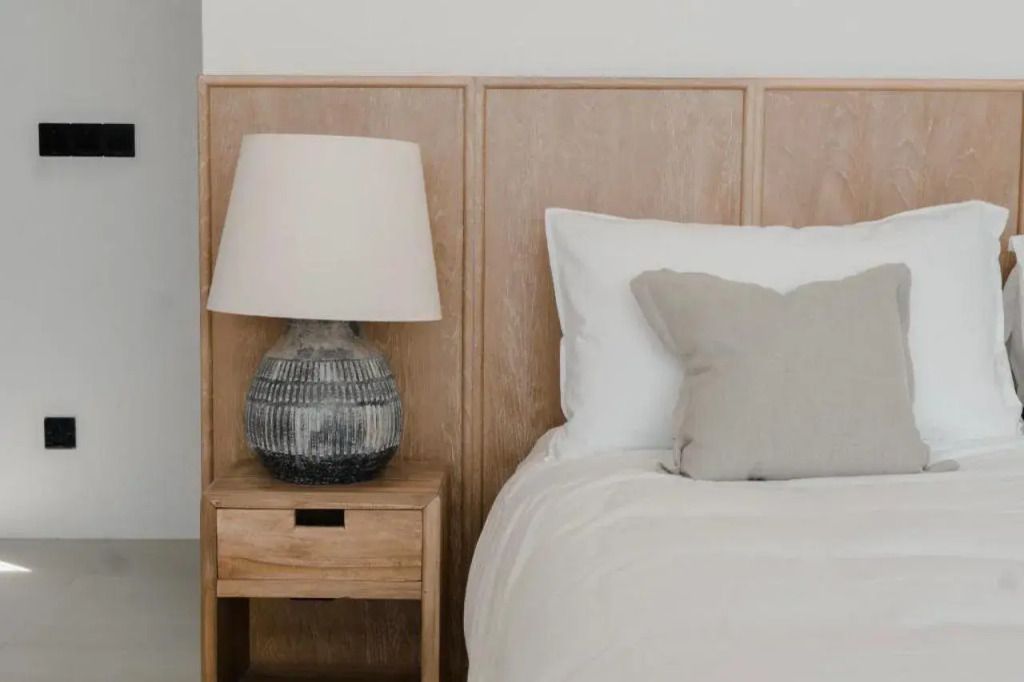 Holz-Nachttisch mit Tischlampe und Kissen auf einem Bett in einem eleganten Zimmer.