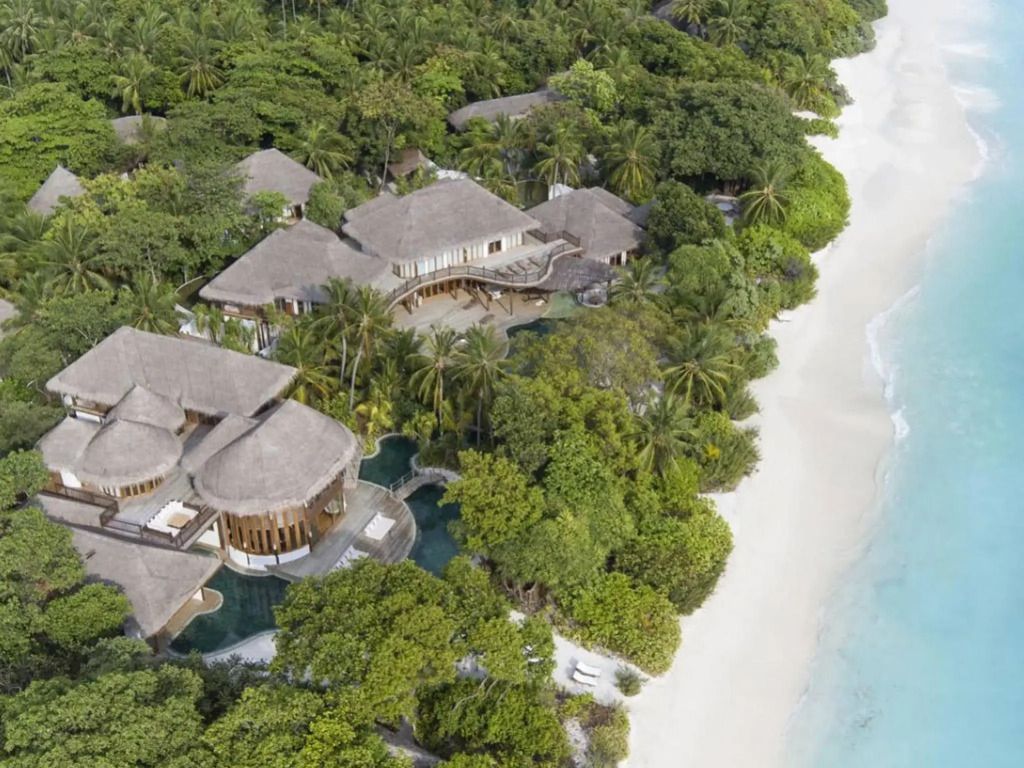 Luftaufnahme von Villen inmitten von üppigem Grün direkt am weißen Sandstrand