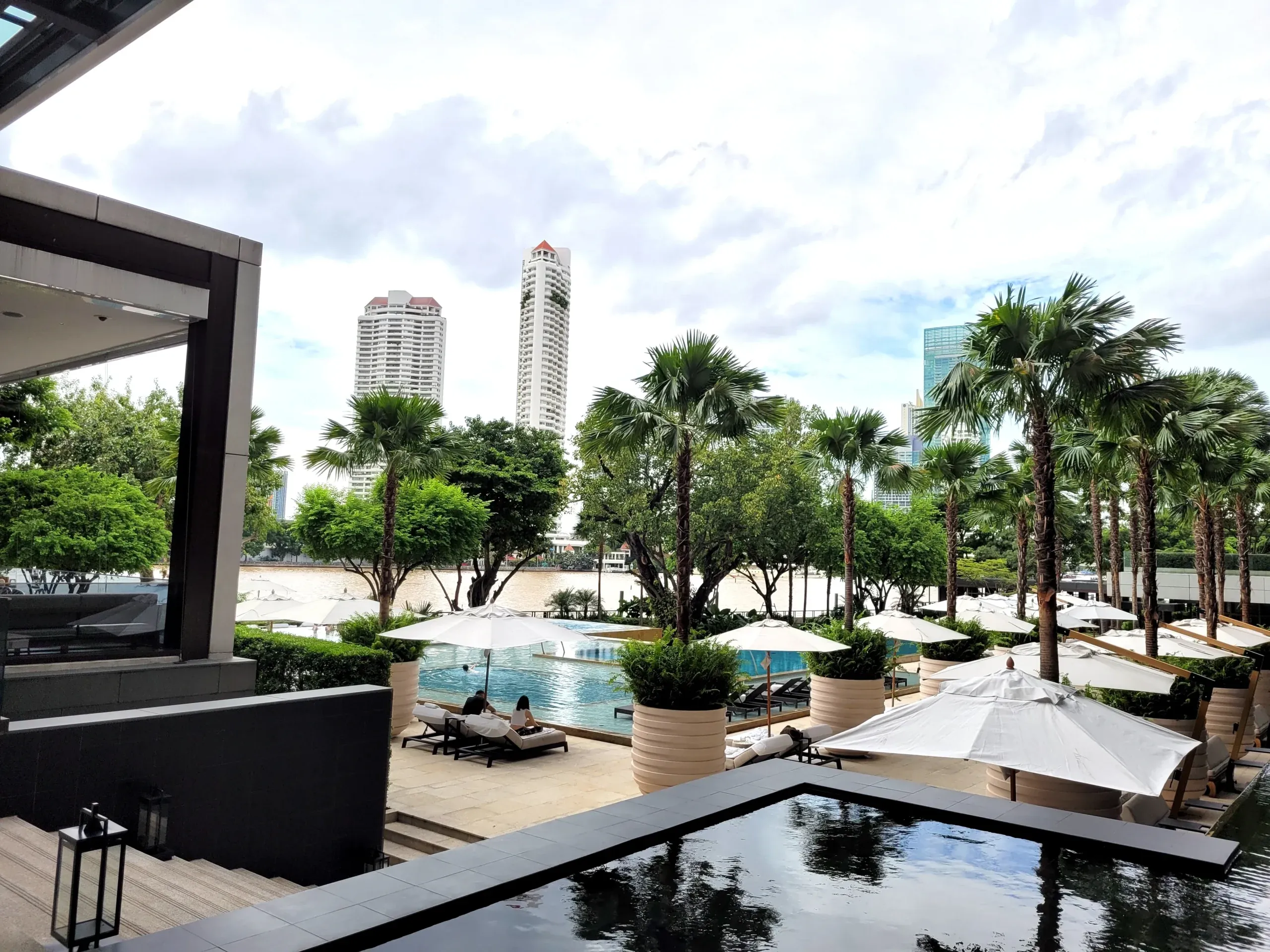 Four Seasons Bangkok Außenbereich mit Pool, Palmen und Blick auf Skyline Gebäude