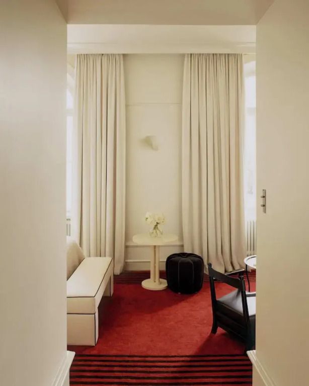 Elegantes Sitzbereich in einem Hotelzimmer mit roten Teppich und Vorhängen.