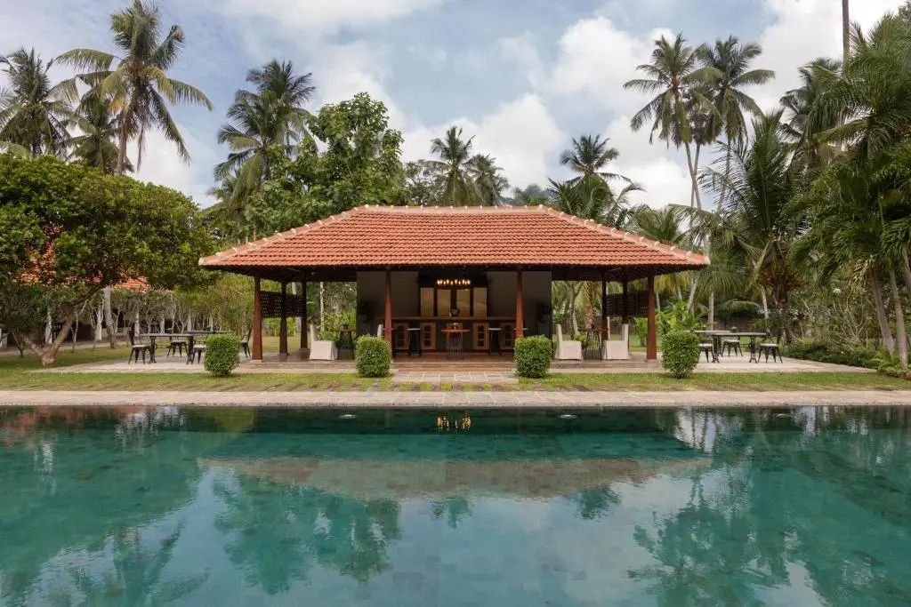 Elegantes Pavillon mit rotem Dach vor einem großzügigen Pool im tropischen Garten