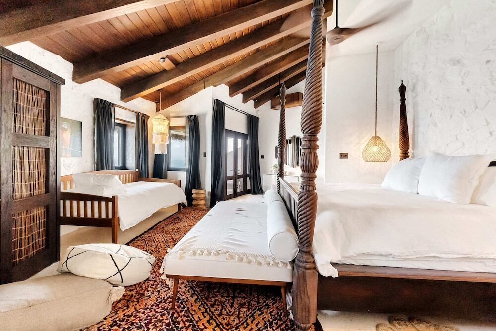 Gemütliches Zimmer mit Holzbalkendecke und zwei Himmelbetten im Boho-Stil