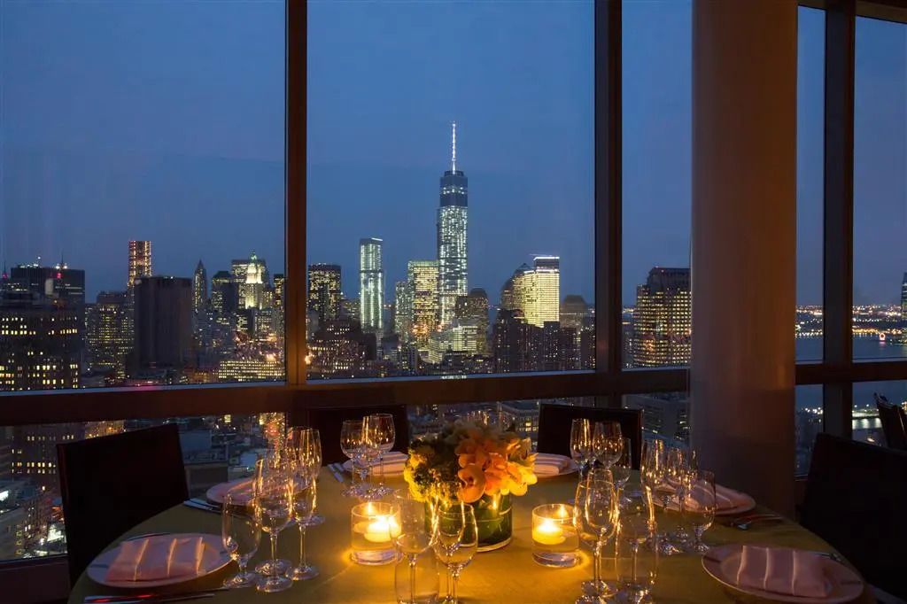 Nächtlicher Blick auf die Skyline von New York City durch großes Fenster eines eleganten Restaurants.