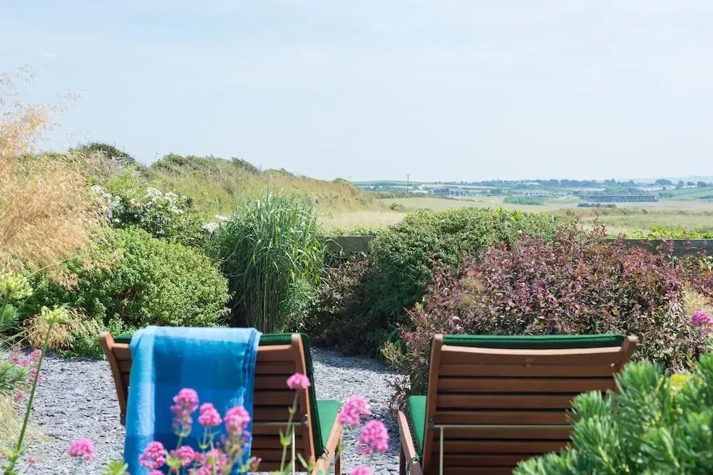 Gartenblick mit zwei Liegestühlen und blühenden Pflanzen im Vordergrund.